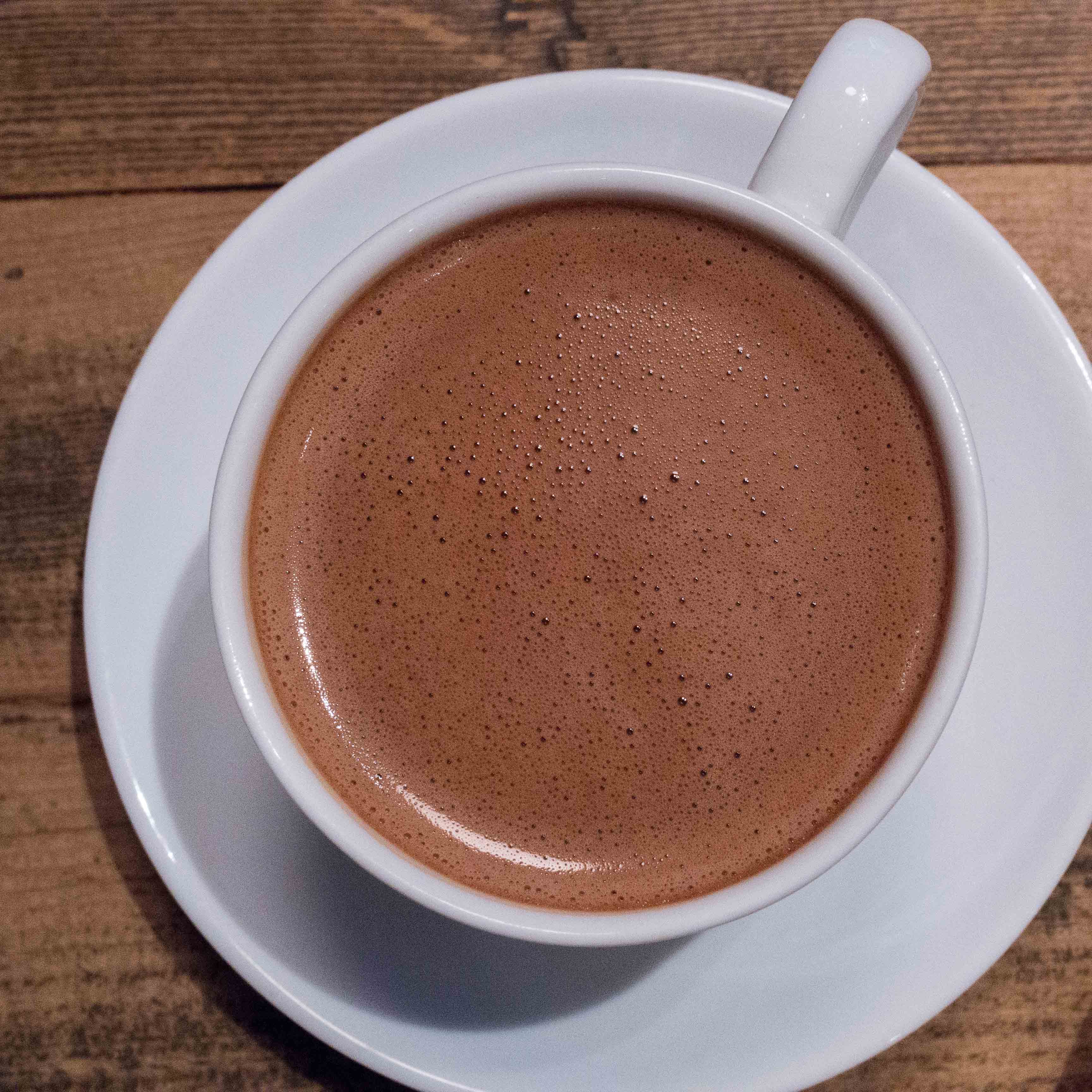 Looking down on a cup of drinking chocolate in a white mug on a white saucer.